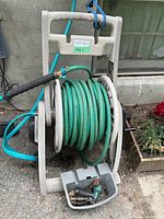 Garden hose coiled on reel with attached spray nozzle and plastic accessory tray with fittings at base