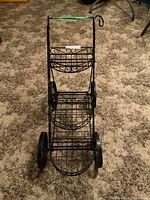 Front view of the black metal plant stand showcasing the three circular shelves and wheels.