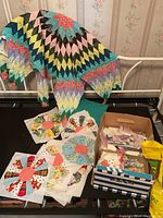 View of large quilt with pastel and bright color diamond patterns hanging over a railing with circular floral blocks and a box of fabric scraps underneath.