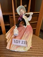 Front-right angle view of the Royal Doulton figurine showing the woman with bonnet, black bodice, peach-yellow skirt, and white muff in hand.