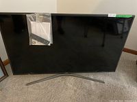 Front view of TV on stand with remote and manual taped to screen