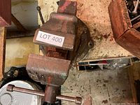 Heavy metal bench vise attached to a workbench surface, showing rust and wear, with a LOT 400 label attached.