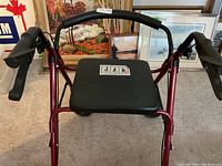 Front view of red walker showing padded seat, hand brakes, and frame structure with four wheels.