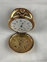 Watch open to display white enamel dial with black Arabic numerals, Waltham logo and sub-seconds at 6