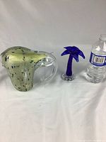 Full view of the two glass figurines side by side with a water bottle for scale showing the bird's size and palm tree.