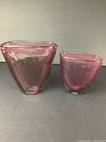 Two hand blown purple art glass vases with organic triangular shapes and thick glass, shown from front