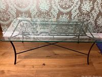 Coffee table viewed from a side angle showing metal frame with decorative elements and glass top