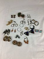 Overview of vintage costume jewelry earrings in various styles and materials displayed on white background.