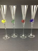 Four crystal champagne glasses with colored snail embellishments, shown standing in a row with different colors, against a dark gray backdrop.
