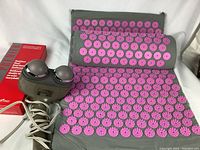 Grey acupuncture mat and pillow with pink massage points, accompanied by HoMedics hand massager visible in photo.