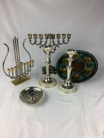 Full view of all Judaica silverplated items including two Menorahs, Passover plate, candlesticks, and candle holder dish shown on white background.
