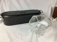 Photo showing black metal fish poacher with lid and clear glass fish-shaped vase on white background.