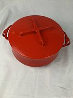 Red enameled cast iron Dutch oven pot with lid, top view showing lid with raised cross handle and side handles on pot.