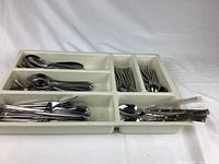 White plastic cutlery tray filled with stainless steel forks, spoons, and knives, showing overall content and organization.