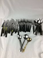 Overview of entire stainless steel cutlery set including knives, forks, spoons, and three small decorative spoons.