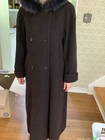 Front view of full length dark purple wool coat with double-breasted buttons and dark fur collar worn by model.