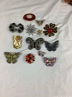 Full lot layout showing all vintage costume brooches on white background, displaying varied designs and colors.