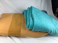 Two folded vintage wool blankets—the blue blanket with minor pilling and the yellow blanket with a gradient effect—lying on a white background.