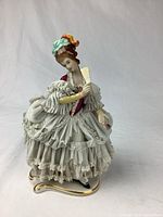 Photo showing full front view of the vintage Dresden porcelain figurine with detailed lace dress and fan, highlighting lace fabric and bonnet with colorful accents.