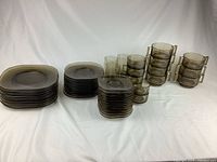 Full overview showing stacks of various sizes of smoked glass plates, bowls, cups, and tumblers.