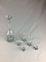 Full view of decanter with stopper and five shot glasses on white background