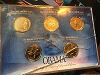 Five collectible coins housed in a display case with each coin representing different years of Barack Obama's life and labeled accordingly.