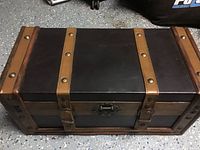 Front and top view of a rectangular wooden chest with three tan leather straps and brass studs, along with a central metal clasp lock.