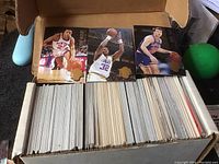 Box filled with over 300 basketball trading cards, three cards displayed on top showing players in action.