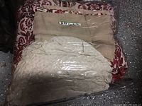 Photo of three folded comforters stacked inside clear plastic packaging. One beige, one red and white damask pattern, one light cream color.