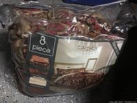 Photo of 8 piece king bed ensemble comforter set in its original zippered packaging showing the intricate, brown-gold reversible pattern.