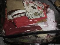 Zipped transparent storage bag containing assorted bedding including a red comforter and floral patterned pieces.