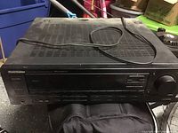 Front view angled image of Curtis Mathis stereo receiver showing power cord resting on top in dusty condition.