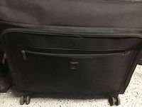 Front view of black soft-sided Delsey luggage showing two zippered pockets and four wheels at bottom