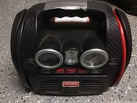 Front view of the black jumpstarter and tire inflator with dual analog gauges and control buttons.