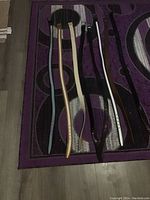 Seven men's leather belts laid out on patterned rug showing various colors and buckle styles.