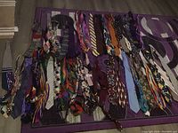 Photo showing a collection of men’s ties arranged on a patterned purple surface, displaying a variety of colors and patterns.