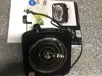 Top view of black electric single burner hot plate with coil element, temperature knob, and indicator lights, placed on its box.