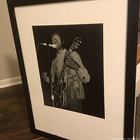 Full view of framed Chuck Berry black and white photographic print in black frame without glass, showing the image of Chuck Berry with guitar and microphone.