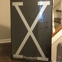 Front view of framed vintage Warner Bros. poster. Large silver X on black background with "November 18" text.