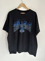 Front view of a black Harley Davidson T-shirt on a wooden hanger showing the flame design and logo.