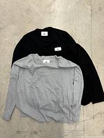 Three sweatshirts laid out flat, one grey, two black, showing overall design and condition.