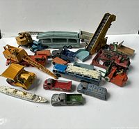 Photo of multiple vintage toy vehicles including Dinky Toys delivery trucks, cranes, buses, a toy ship, and other metal toy cars from London Toy.