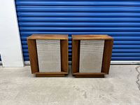 Pair of vintage walnut speaker cabinets with fabric grills photographed against a storage unit blue door