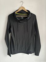 Full view of black women's long sleeve top hanging on wooden hanger, showing fitted design and high collar with drawstring.