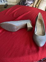 Bandolino silver dress shoe shown on red surface, highlighting textured metallic silver upper and block heel.