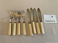 Full set of 4 fish knives and 4 fish forks showing cream-coloured handles and silver decorative collars.