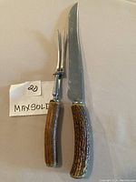 Carving knife and fork with wood-like handles on white surface with MAXSOLD tag