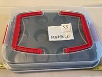 Closed cupcake carrier with red handles visible on top, showing the container's size and protective lid.