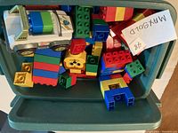 Photo showing an open Rubbermaid Roughneck box filled with assorted Duplo blocks and a white toy vehicle.