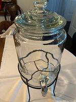 Full view of clear glass beverage dispenser on black metal stand with chrome tone tap near base.